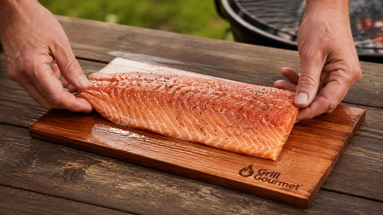 Hands placing a raw salmon fillet skin-side down onto a soaked cedar plank before grilling