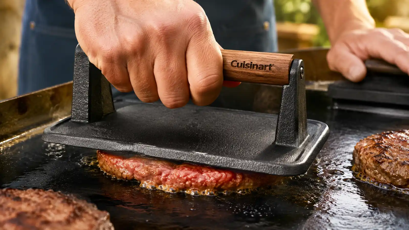 Hand pressing a smash burger patty flat on a griddle with the cast iron press