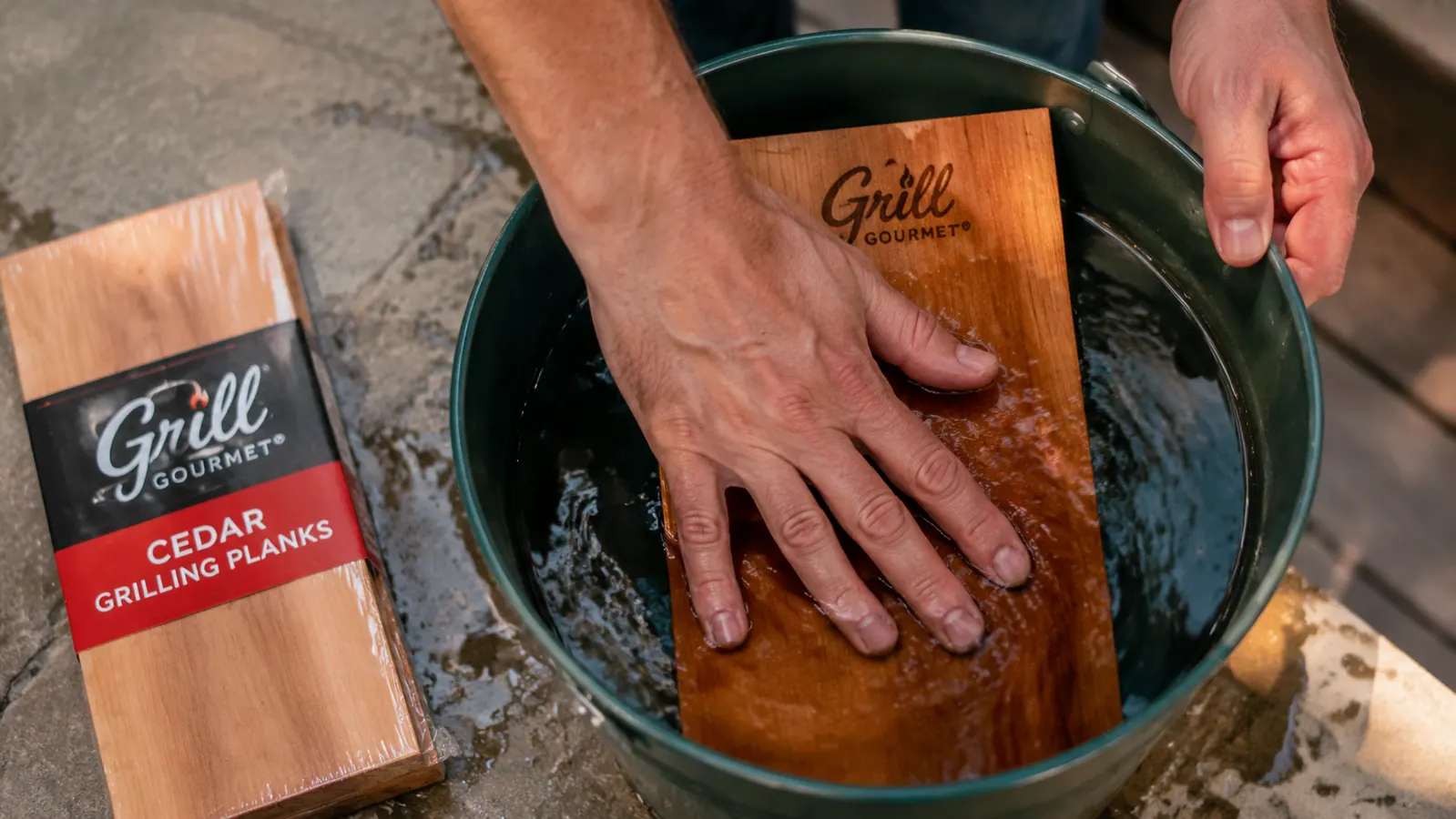 Hand testing whether a soaked cedar plank sinks in a bucket of water on a porch step