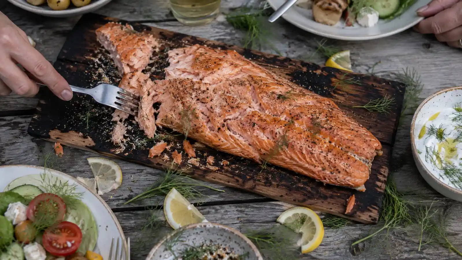 Finished cedar plank salmon fillet flaking apart on a wooden serving board next to lemon wedges